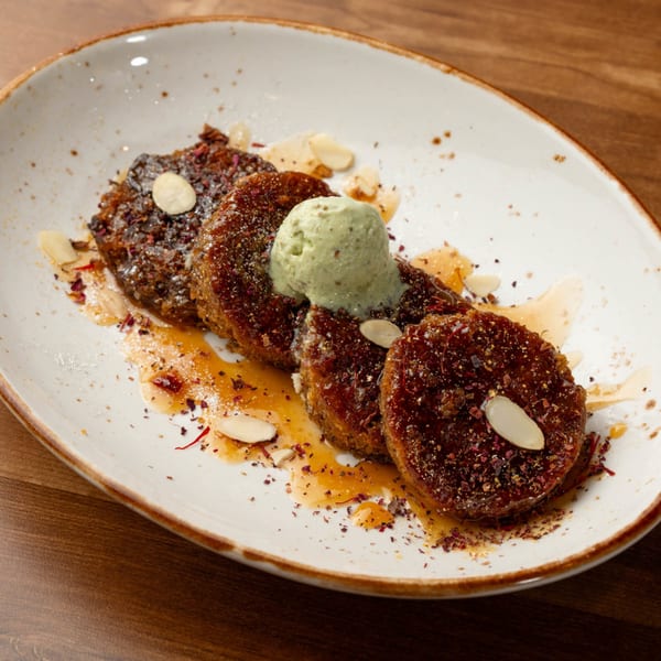 Four Indian desserts, possibly Gulab Jamun, with green ice cream, syrup, and almond slivers.