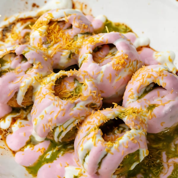 Close-up of Indian Dahi Puri, topped with pink and white yogurt, green chutney, and sev.