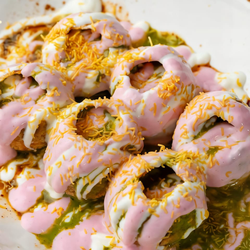 Close-up of Indian Dahi Puri, topped with pink and white yogurt, green chutney, and sev.
