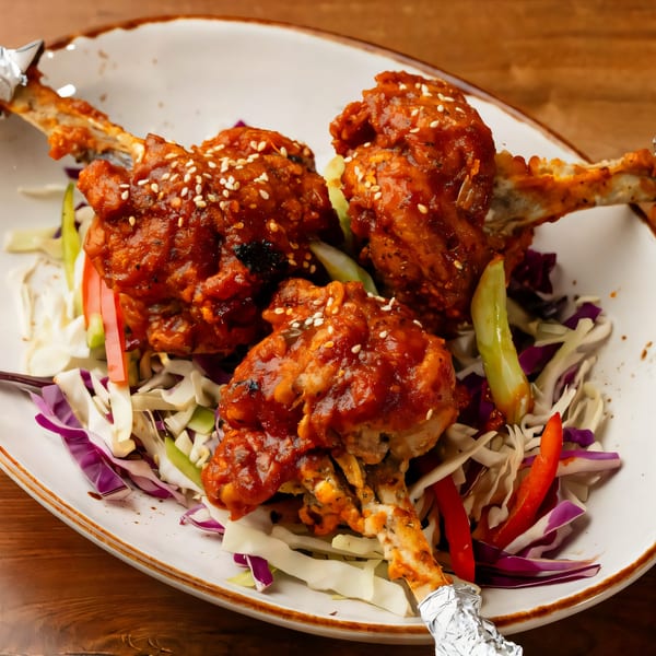 Three Indian chicken lollipops with sesame seeds, red sauce, and shredded cabbage on a white plate.