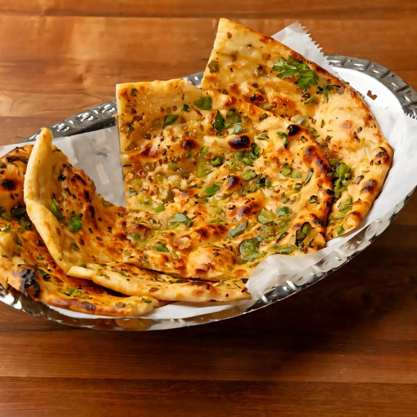 Golden Indian garlic naan bread, garnished with green herbs, served in a silver basket on a wooden table.