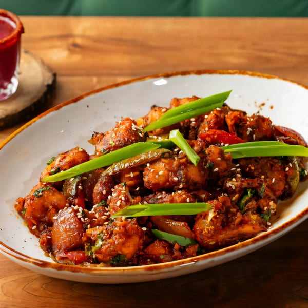 A plate of Indian chili chicken, garnished with sesame seeds and green onions, on a wooden table.