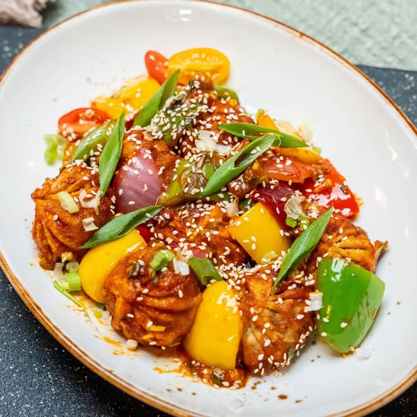 Indian chili momos with bell peppers, onions, and sesame seeds on a white plate.