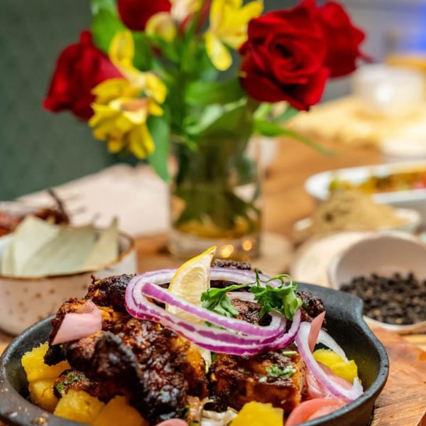 Indian dish with grilled meat, pineapple, red onions, and lemon, with flowers in the background.